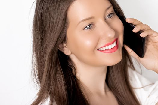 Happy suntanned woman smiling and calling on smartphone on holiday, portrait on white background. People, technology and communication concept.