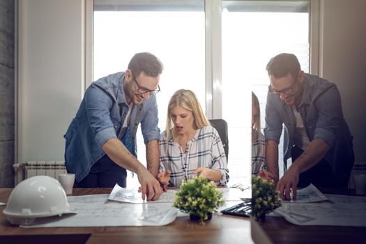 Young successful architect colleagues talking and analyzing blueprints while working on a new project at the office.