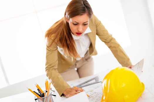 Young woman architect constructor analyzing blueprint at desk in office. 