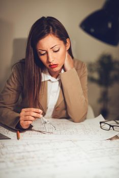 Successful young thoughtful female architect think how to solve the problem on blueprint.