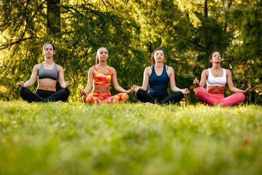 Fitness group of four young women doing yoga meditation in the city park.