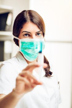Young female nurse standing in her consulting room and preparing an injection of Anesthesia. Selective focus. Focus on background, on nurse.