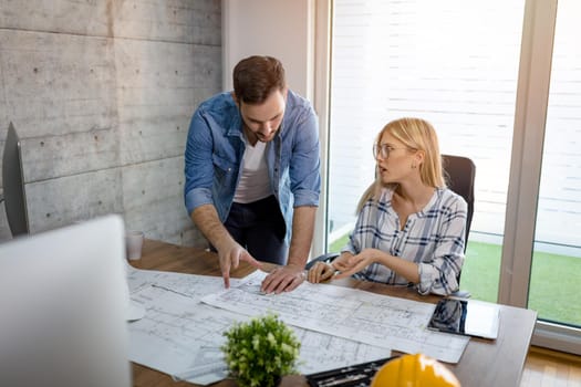 Young architect colleagues talking and analyzing blueprints while working on a new project at the office.