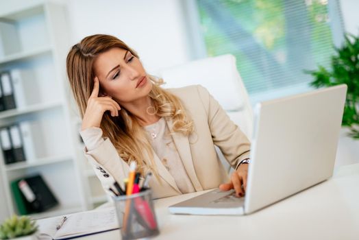 Young pensive business woman thinking about the best possible solutions, while working on her laptop in the office.