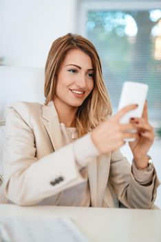 Young pretty smiling businesswoman texting message on the smartphone in the office. 