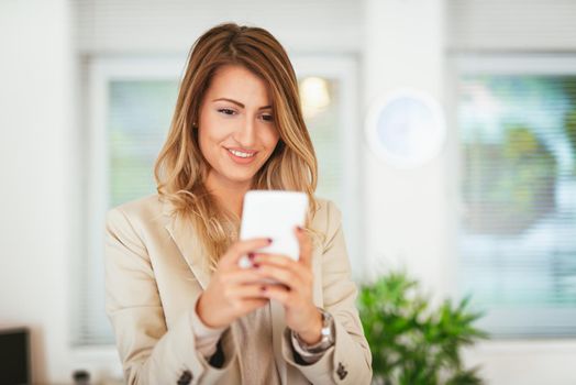 Young pretty smiling business woman texting on the smartphone in the office. 