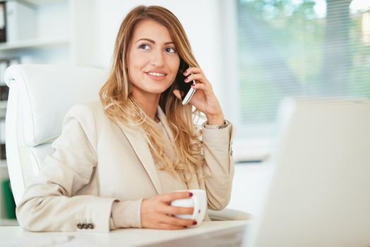 Thoughtful serious young woman lost in thoughts using smartphone, pondering question at work, holding cup of coffee. 