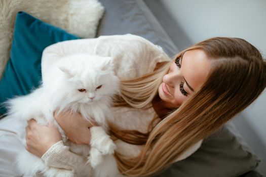 Cute young woman relaxing at home and embracing her beautiful white Persian cat. Top view.