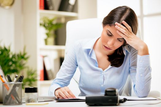 Worried young woman in the office brainstorming over business report.