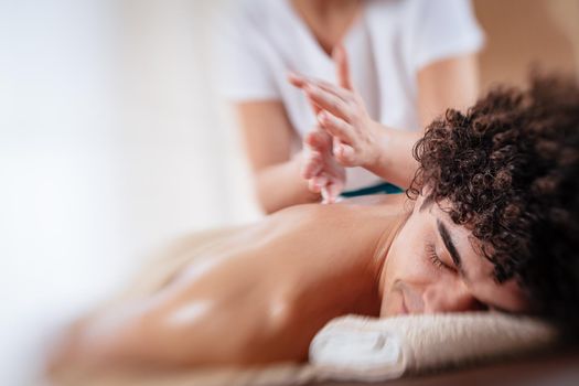 Close-up of a handsome healthy young man enjoying relaxing back massage at beauty salon. Selective focus.
