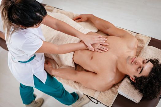 Handsome man lying down on his back, getting healthy massage by young female therapist, in spa center.