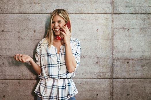 Young beautiful successful female entrepreneur talking on a smart phone in front of a concrete wall.