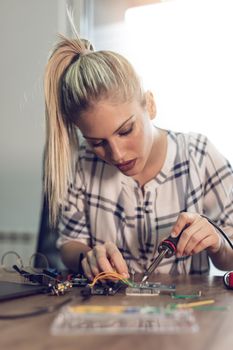 Young woman technician focused on the repair of electronic equipment by soldering iron.