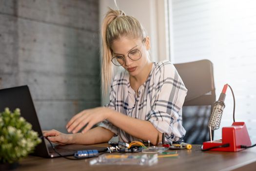 Young woman technician focused on the repair of electronic equipment cecking something on the laptop.