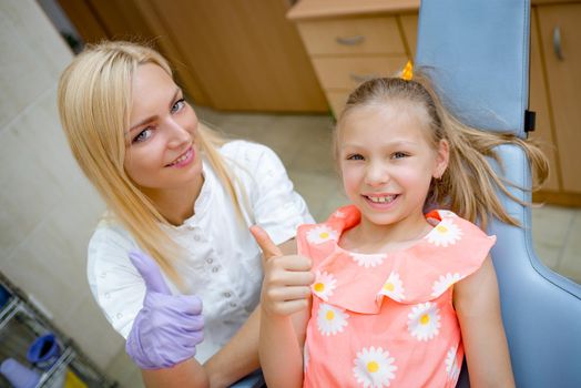 Little girl smiling with the dentist, satisfied after polishing her teeth at the pediatric dental office. Looking at camera.