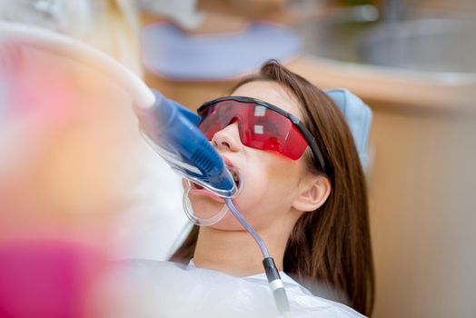 Close-up of beautiful young woman in visit at the dentist office, whitening teeth with ultraviolet light.