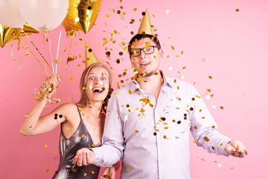 Birthday party. Funny couple celebrating birthday. Happy laughing couple celebrating birthday party holding golden balloons and gift box, throwing golden confetti