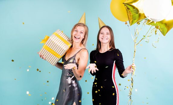 Birthday party. Two young women in birthday hats holding balloons celebrating birthday over blue background