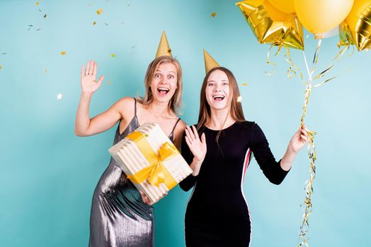 Birthday party. Two young women in birthday hats holding balloons celebrating birthday over blue background