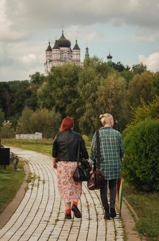 Girlfriends hold hands and walk in the park, a young lesbian couple walk outdoors with a rainbow umbrella