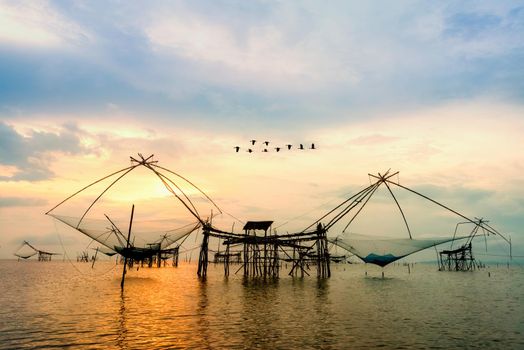 Beautiful nature landscape golden light of the morning sky at sunrise with flock of birds are flying over the native fishing tool, rural lifestyle at Pakpra canal, Baan Pak Pra, Phatthalung, Thailand