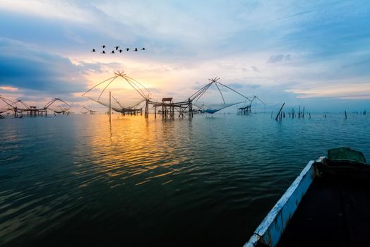 Beautiful nature landscape golden light of the morning sky at sunrise with flock of birds are flying, native fishing tool and prow, rural lifestyle at Pakpra canal, Baan Pak Pra, Phatthalung, Thailand