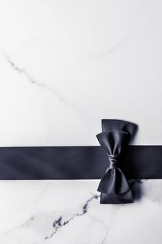 Holiday gift, decoration and sale promotion concept - Black silk ribbon and bow on marble background, flatlay