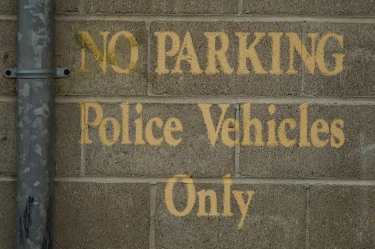 A No Parking zone used for police vehicles only is painted on the brick wall outside a courthouse parking lot.