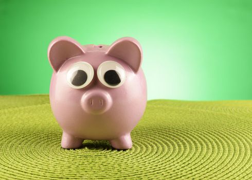 A piggy bank with some funny googly eyes in a green environment surrounding.