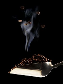 A scoop of freshly roasted coffee beans over a dark black background.