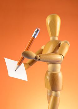 An Artists wooden Dummy Mannequin using a pencil and piece of paper to draw or write something of interest while over an orange color background.