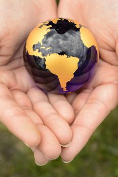 The Earth Globe is safely held inside the palm of a womans hands overtop of a grass area.