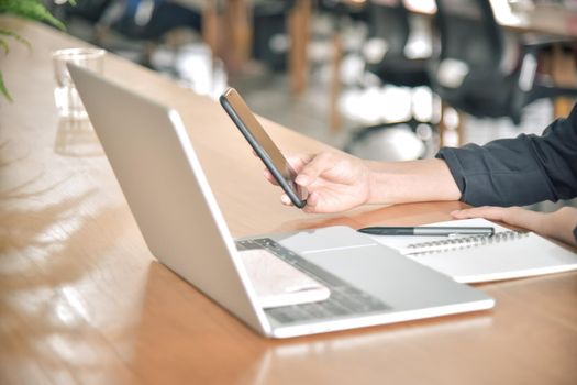 Young businesswoman using smart phone on her desk at the workplace, closeup