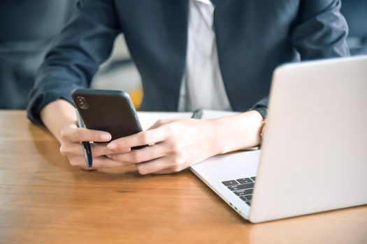 Young businesswoman using smart phone on her desk at the workplace, closeup