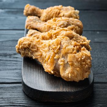 Crispy fried chicken cuts on black wooden background.