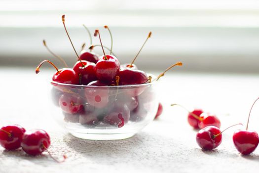Cherry berry in a vase. Cherry berry in a transparent plate on a light background . Summer red berries. Article about berries.