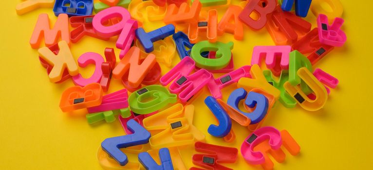 multicolored plastic english alphabet letters with magnet on yellow background, banner