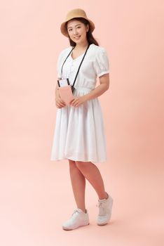 Fun travel portrait of smiling young beautiful Asian tourist woman holding passport isolated on pink background