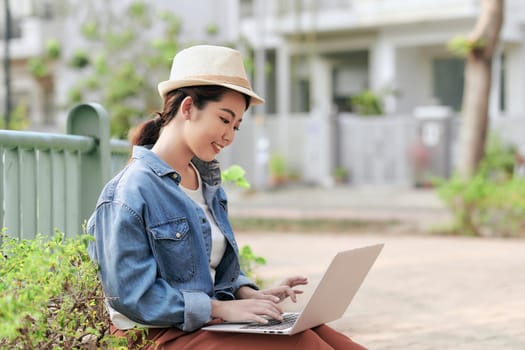 Smiling young girl making notes in notepad while sitting outdoors with laptop computer
