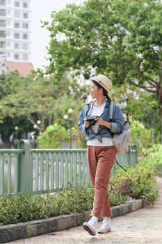 Young pretty cheerful girl posing on the street at sunny day, having fun alone, young photographer with vintage camera.