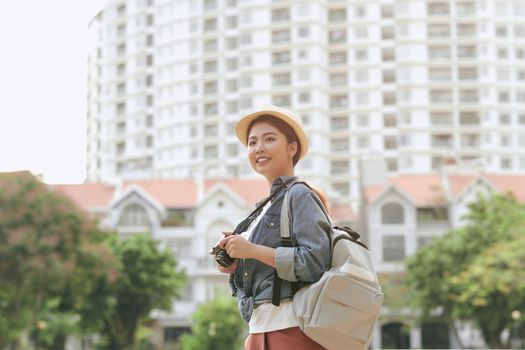 Young beautiful Asian backpack traveler woman using digital compact camera and smile, looking at copy space. 