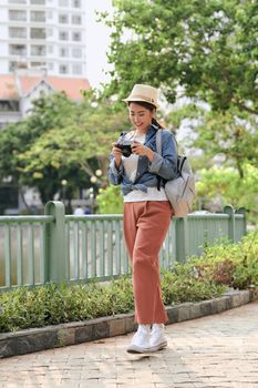 Young beautiful Asian backpack traveler woman using digital compact camera and smile, looking at copy space. 