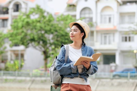 Tourist with travel guide book. Young woman traveler smiling happy.