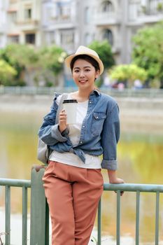 Portrait of an attractive smiling student woman. Young hipster girl holding cup of coffee in the city