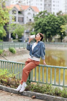 Happy young woman enjoying drinking coffee against urban background.