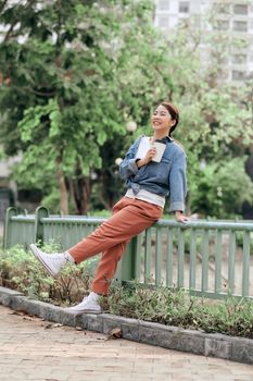 Happy young beautiful woman holding coffee cup in hands and smiling while sitting on city street