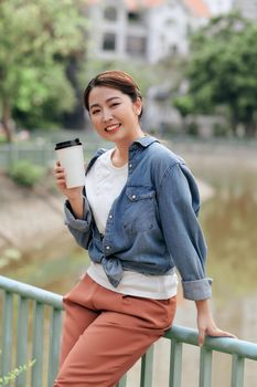 Happy young woman enjoying drinking coffee against urban background.