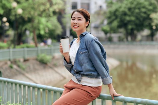 Beautiful young woman with a disposable coffee cup, drinking coffee in her hands against city office.