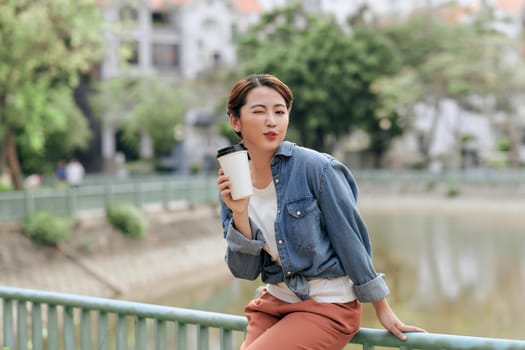 Portrait of an attractive smiling student woman. Young hipster girl holding cup of coffee in the city