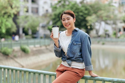 portrait of cheerful happy asian woman satisfied with coffee break holding cup and laughing on street